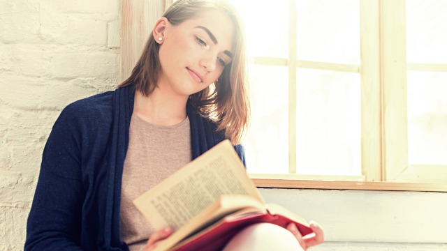 Beautiful young woman reading book at home